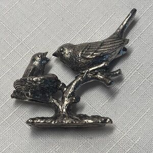 pewter figurine features a parent bird feeding a chick in a nest. high detail